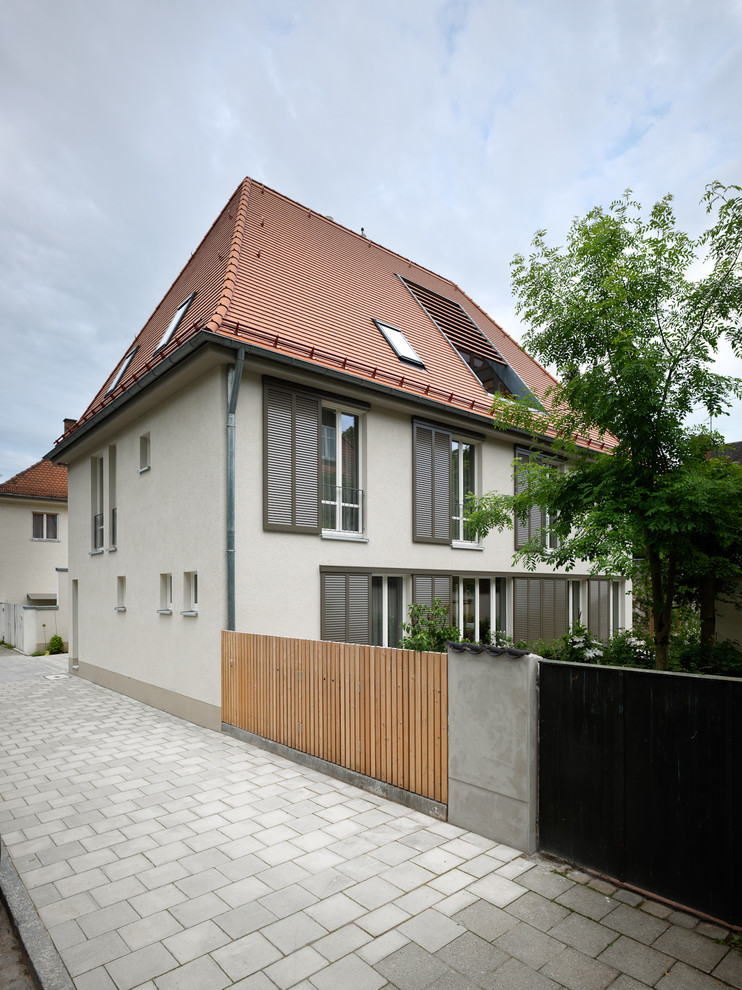 This is an example of a medium sized and beige traditional house exterior in Munich with three floors and a hip roof.