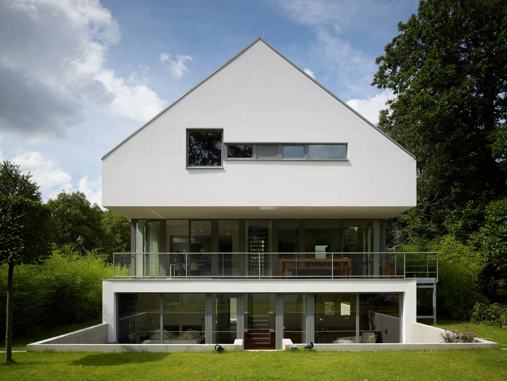 На фото: трехэтажный, белый дом в современном стиле с двускатной крышей с