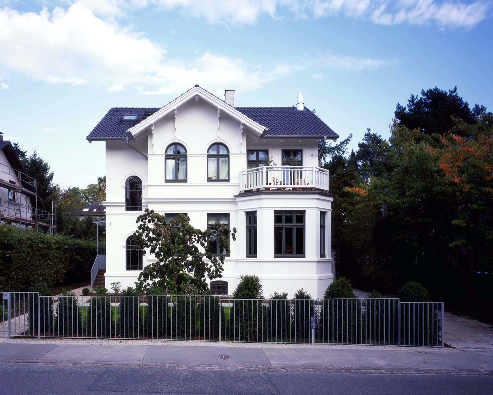 Modelo de fachada blanca de estilo de casa de campo de tamaño medio de tres plantas con tejado a dos aguas y revestimiento de estuco