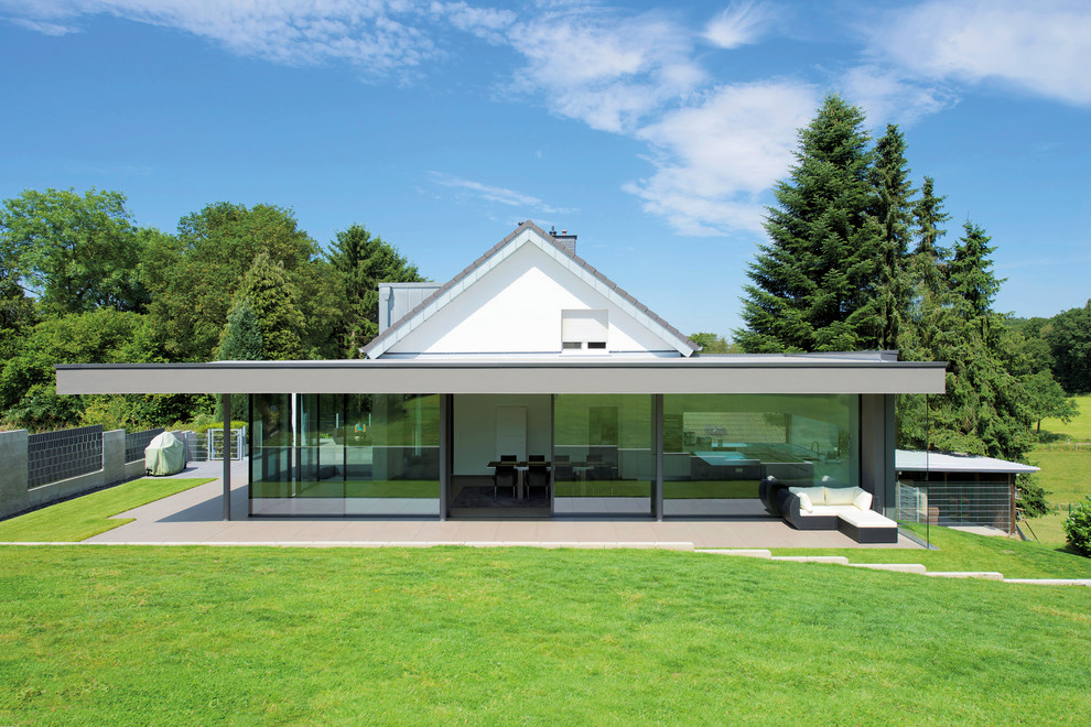 Foto della villa grande bianca moderna a un piano con rivestimento in vetro, tetto a capanna e copertura in tegole