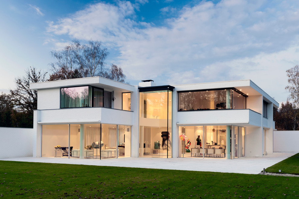 Стильный дизайн: двухэтажный, белый, большой частный загородный дом в стиле модернизм с облицовкой из цементной штукатурки и плоской крышей - последний тренд