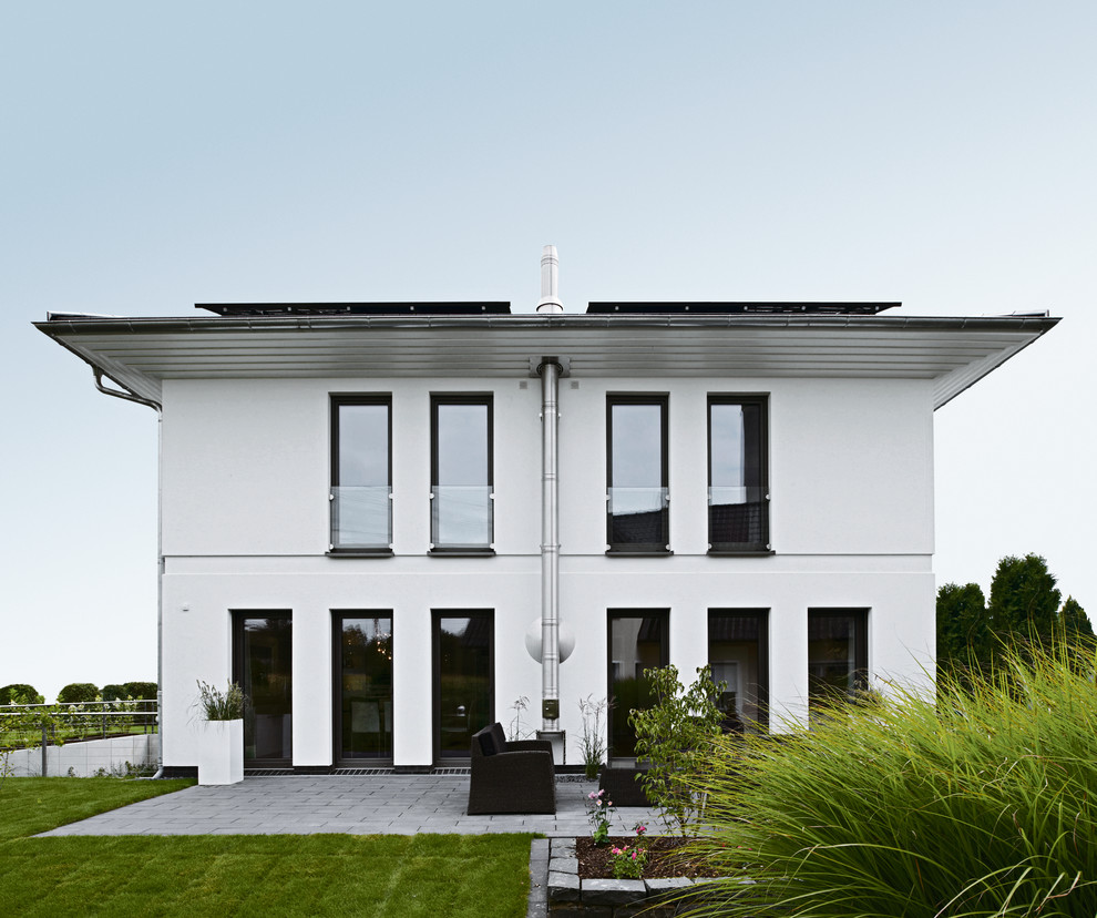 Cette photo montre une grande façade de maison blanche moderne en stuc à un étage avec un toit plat et un toit en tuile.