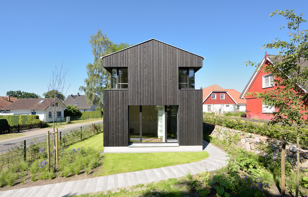 Ejemplo de fachada negra moderna de tamaño medio de dos plantas con revestimiento de madera y tejado a dos aguas