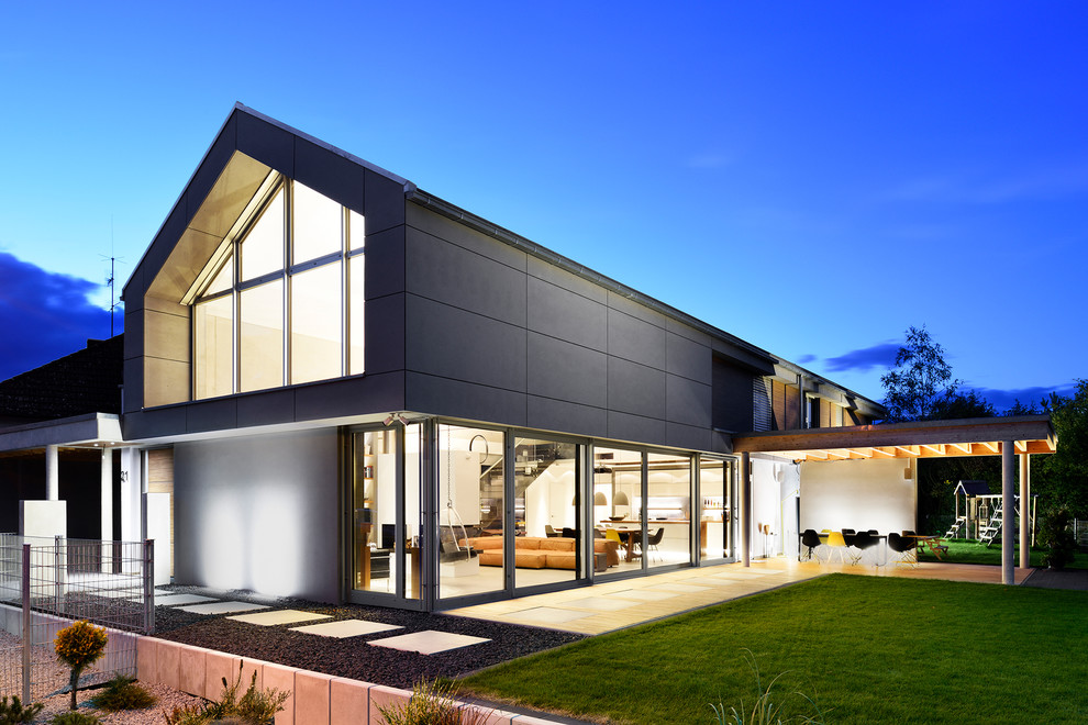 Cette image montre une façade de maison grise design en verre à un étage avec un toit à deux pans et un toit en tuile.