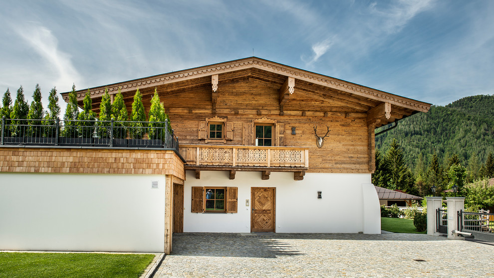 Foto della villa ampia marrone country a due piani con tetto a capanna, copertura in tegole e rivestimenti misti