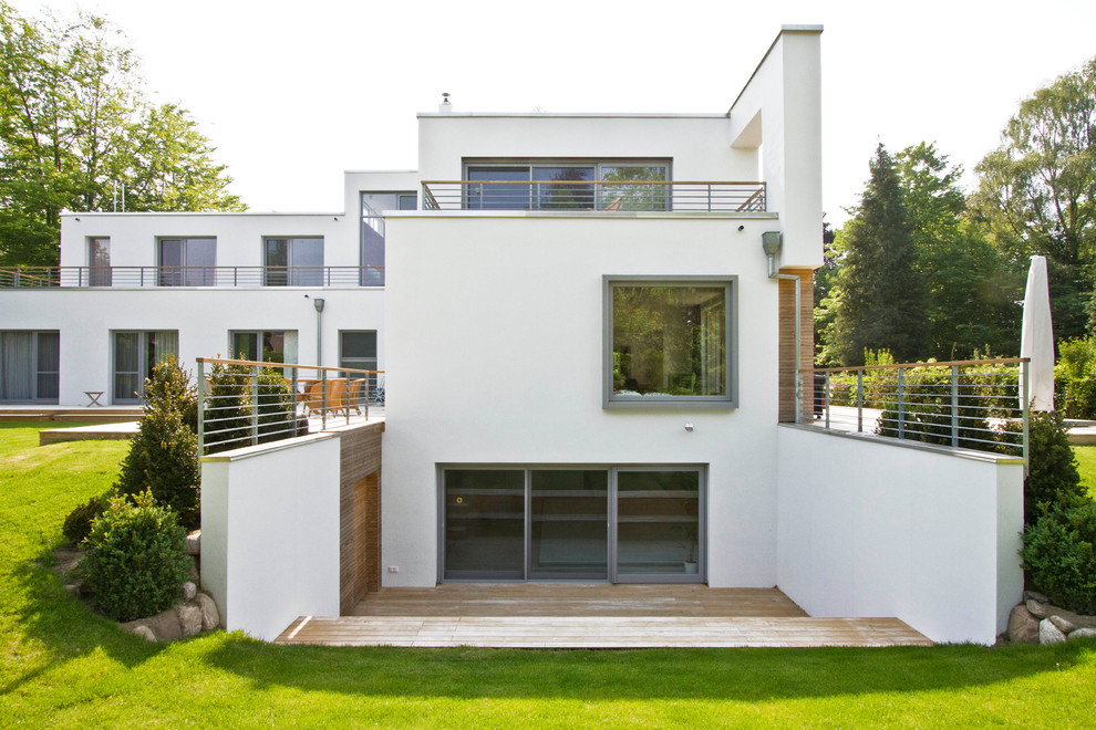 Пример оригинального дизайна: трехэтажный, белый, большой дом в стиле модернизм с плоской крышей и облицовкой из цементной штукатурки