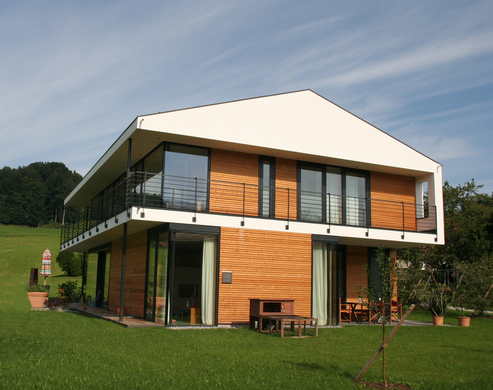 Photo of a large and white contemporary two floor house exterior in Munich with wood cladding and a pitched roof.
