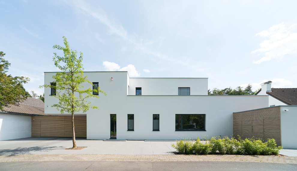 Mittelgroßes, Zweistöckiges Modernes Einfamilienhaus mit Putzfassade, weißer Fassadenfarbe und Flachdach in Düsseldorf