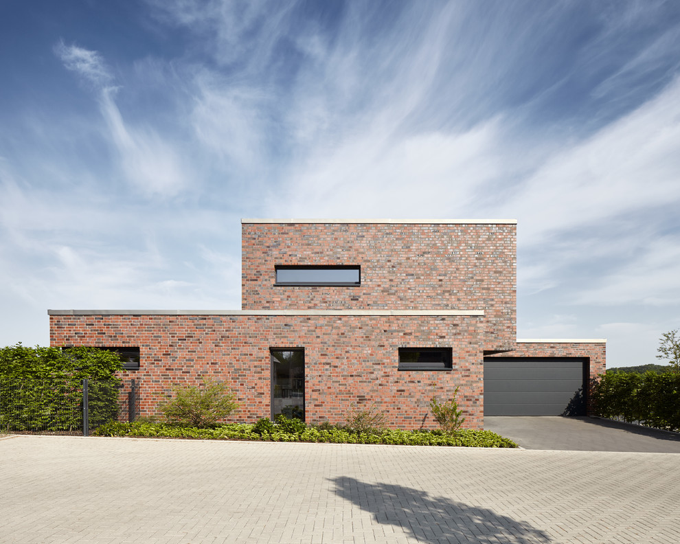 Mittelgroßes, Zweistöckiges Modernes Einfamilienhaus mit Backsteinfassade, roter Fassadenfarbe und Flachdach in Düsseldorf