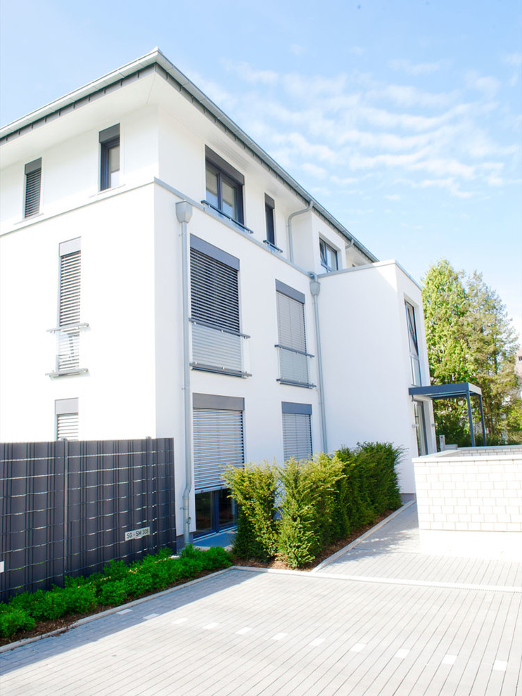 This is an example of a large and white contemporary house exterior in Dusseldorf with three floors and a hip roof.