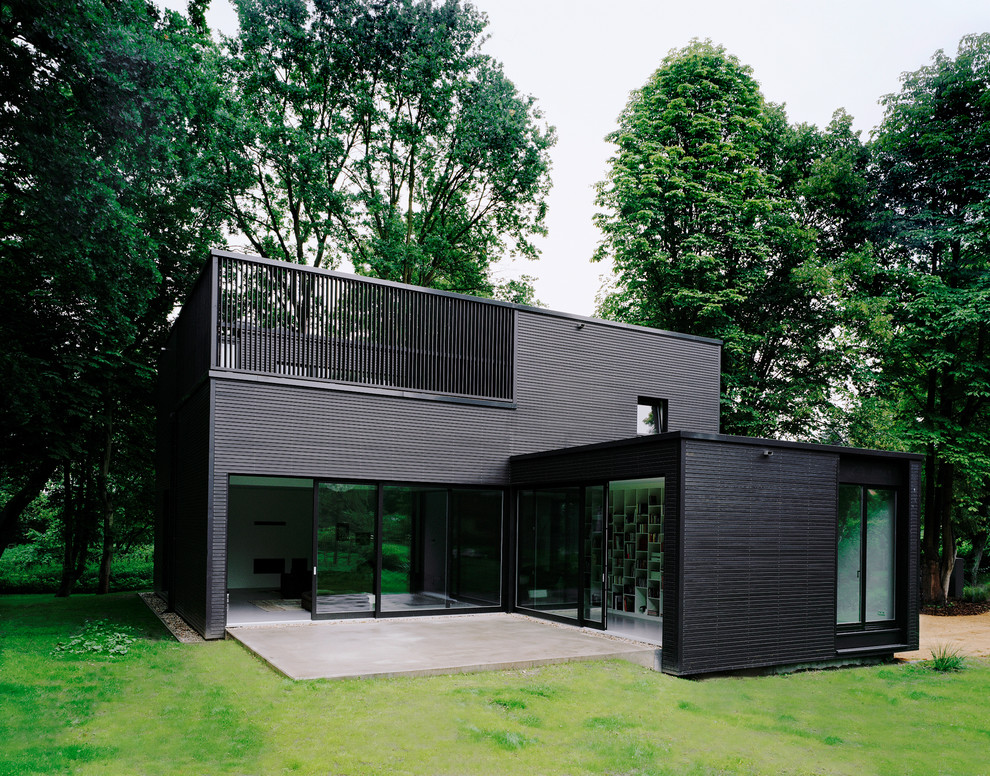 Ejemplo de fachada negra minimalista de tamaño medio de dos plantas con revestimientos combinados y tejado plano