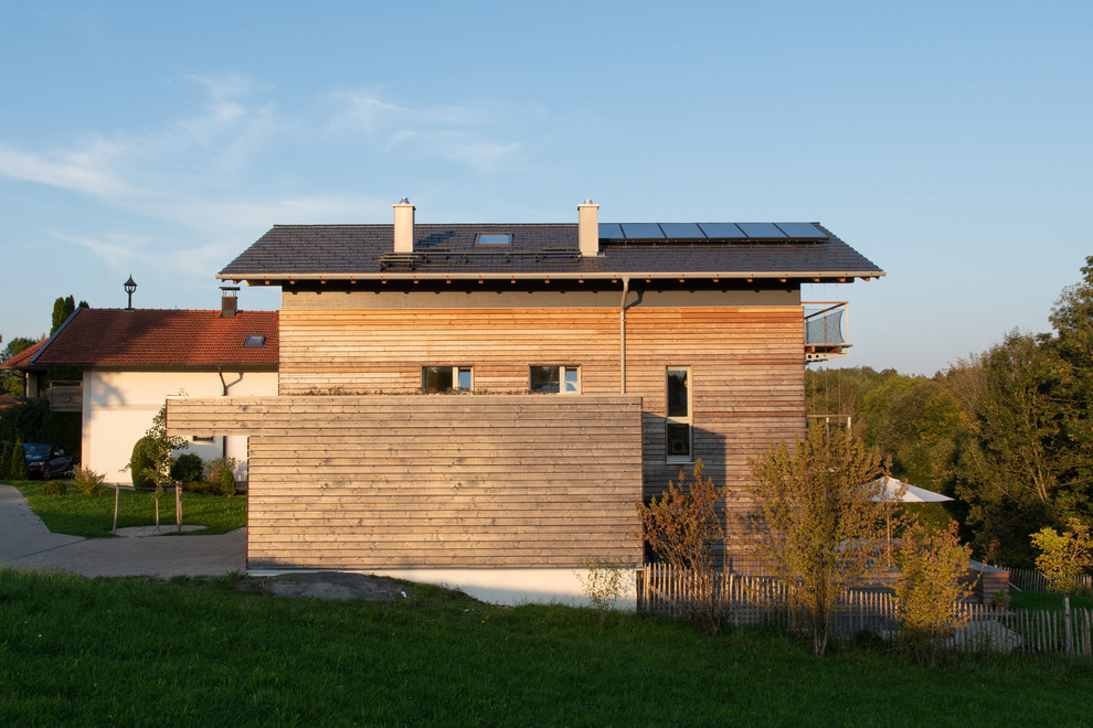 This is an example of a medium sized scandinavian split-level detached house in Munich with wood cladding, a pitched roof and a tiled roof.