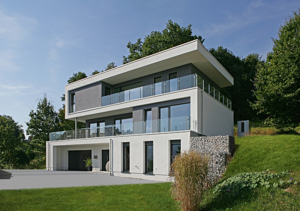 This is an example of an expansive and gey contemporary concrete house exterior in Munich with three floors and a flat roof.