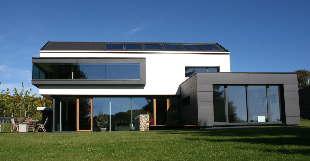 Foto della facciata di una casa grande bianca contemporanea a tre piani con rivestimento in cemento e tetto a capanna