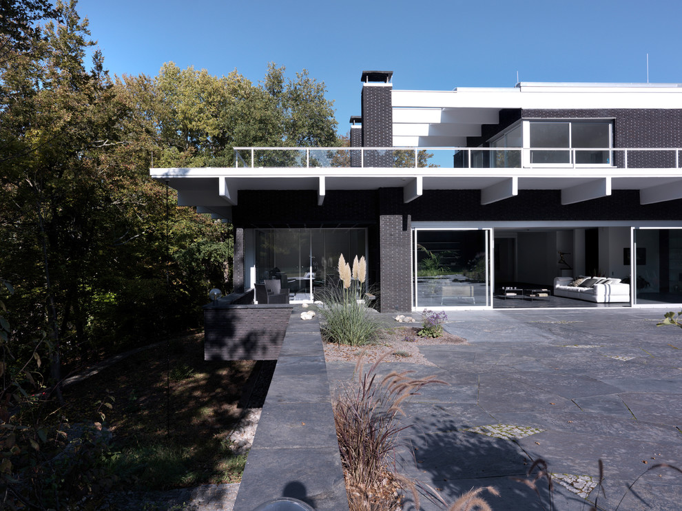 Cette image montre une grande façade de maison noire minimaliste en brique à un étage avec un toit plat.