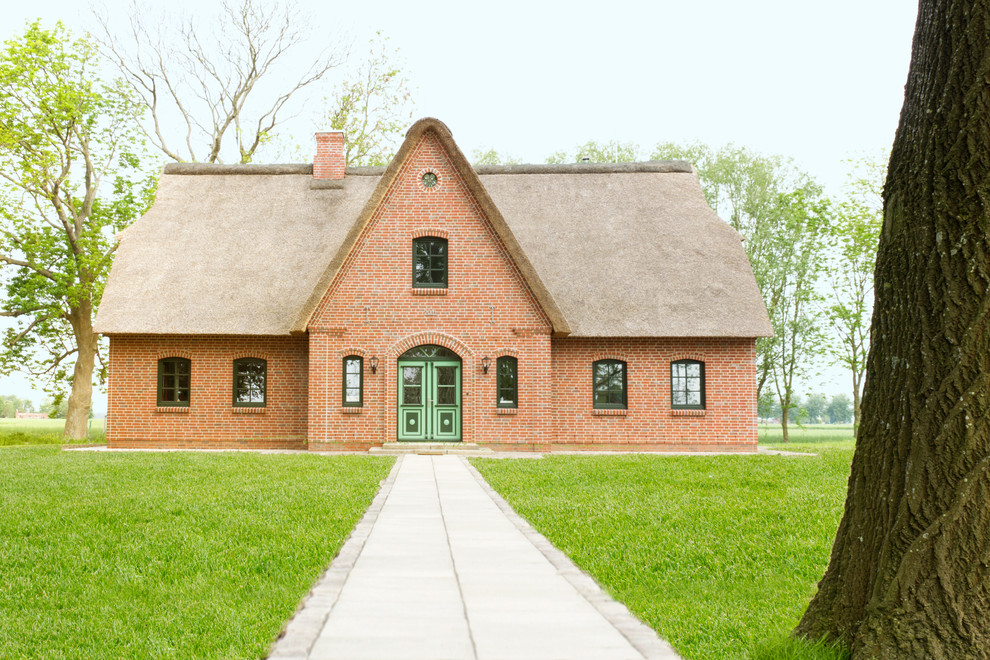 Réalisation d'une façade de maison rouge tradition en brique à un étage et de taille moyenne avec un toit à deux pans.