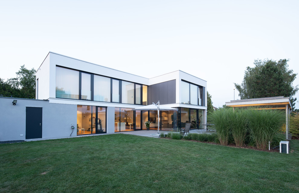 Пример оригинального дизайна: двухэтажный, белый, большой частный загородный дом в стиле модернизм с плоской крышей, зеленой крышей и облицовкой из цементной штукатурки