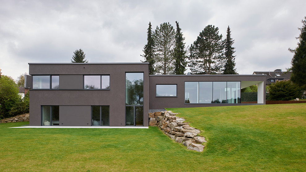Cette photo montre une façade de maison marron moderne en stuc de taille moyenne et à un étage avec un toit plat.