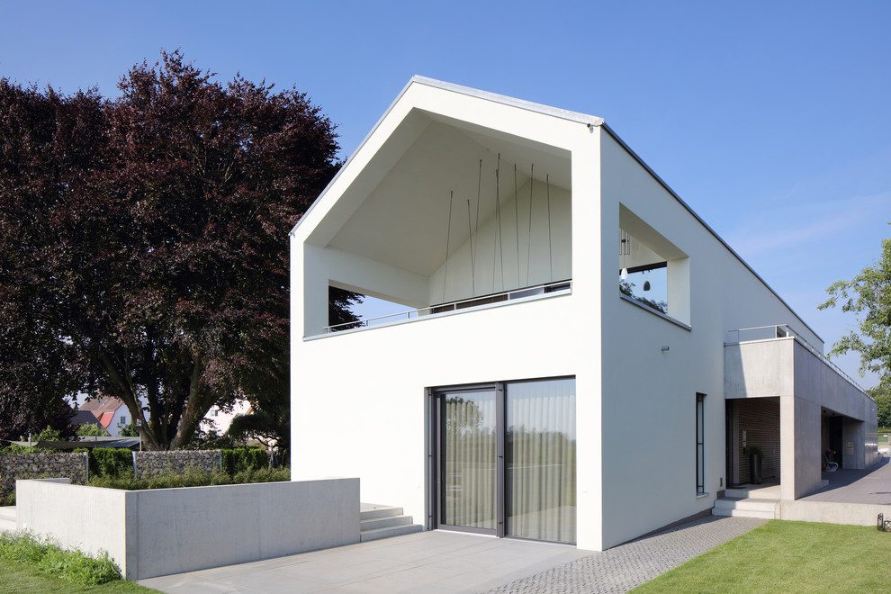 Стильный дизайн: большой, двухэтажный, белый дуплекс в стиле модернизм с двускатной крышей, черепичной крышей и облицовкой из цементной штукатурки - последний тренд