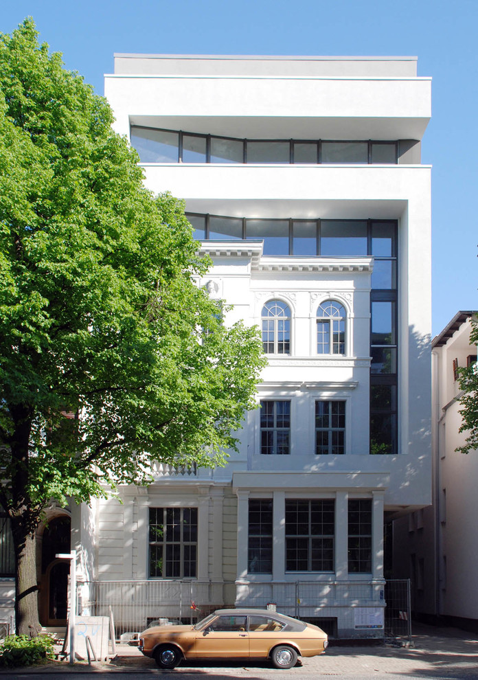 This is an example of a large and white bohemian render house exterior in Hamburg with three floors and a flat roof.