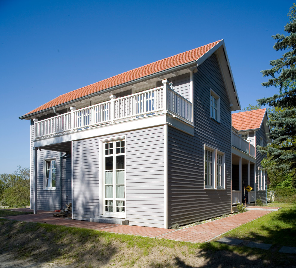 На фото: двухэтажный, деревянный, серый частный загородный дом в стиле кантри с черепичной крышей