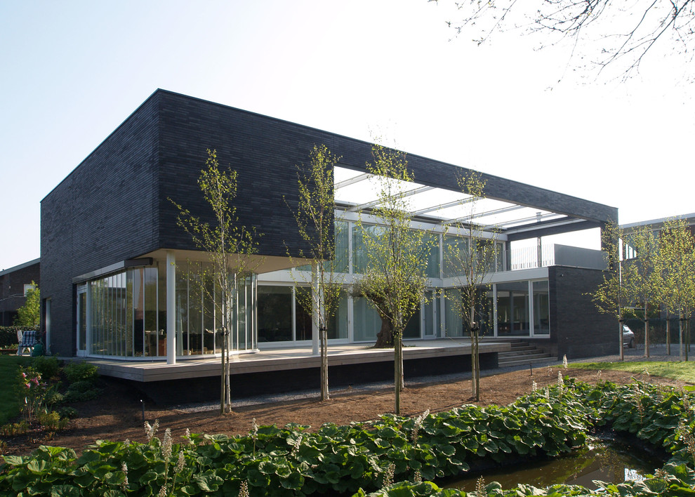 Cette photo montre une très grande façade de maison marron tendance en brique à un étage avec un toit plat.