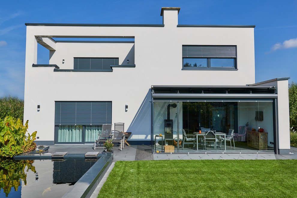 Foto della villa ampia bianca contemporanea a due piani con rivestimento in stucco, tetto piano e copertura verde