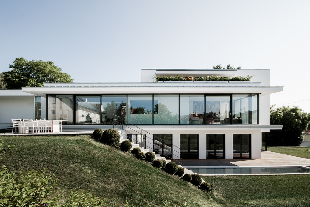 Imagen de fachada de casa blanca minimalista grande de tres plantas con revestimiento de estuco, tejado plano y tejado de metal