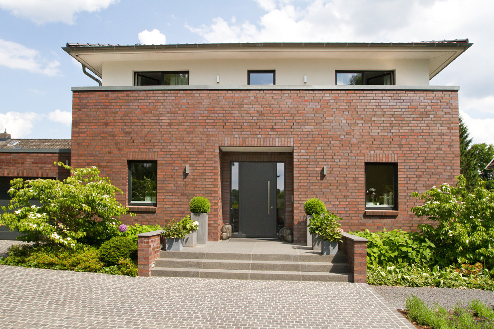 This is an example of a red and large contemporary two floor brick detached house in Hamburg with a hip roof and a tiled roof.