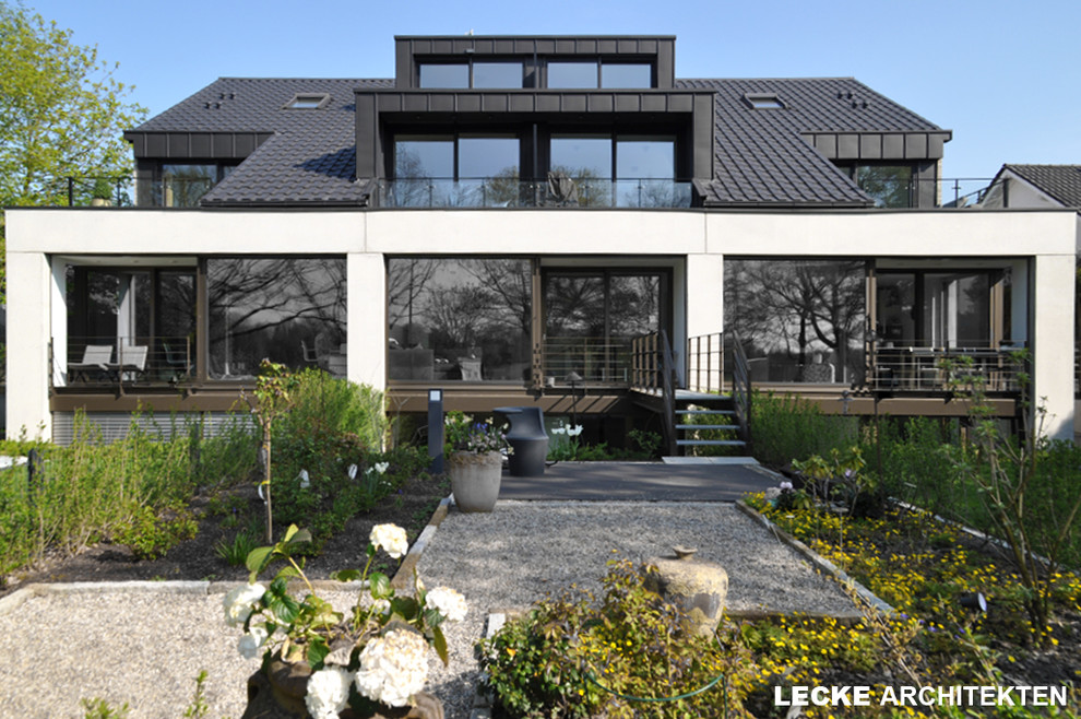 Foto på ett stort funkis grått hus, med tre eller fler plan, tegel, sadeltak och tak med takplattor