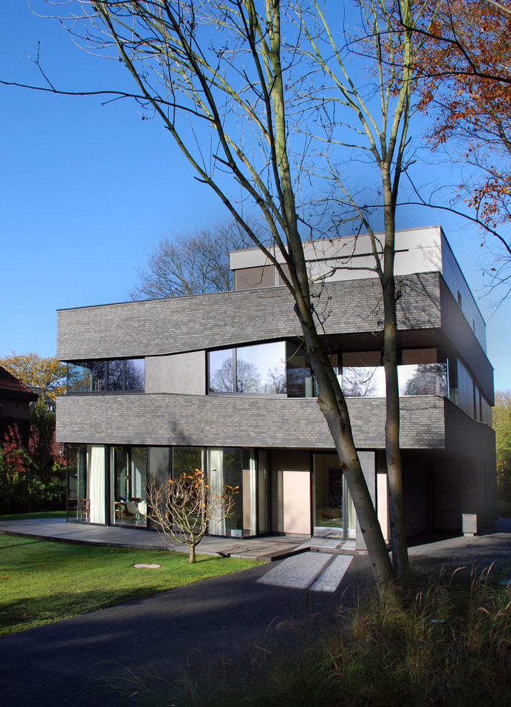 Modelo de fachada gris contemporánea grande de tres plantas con revestimiento de ladrillo y tejado plano
