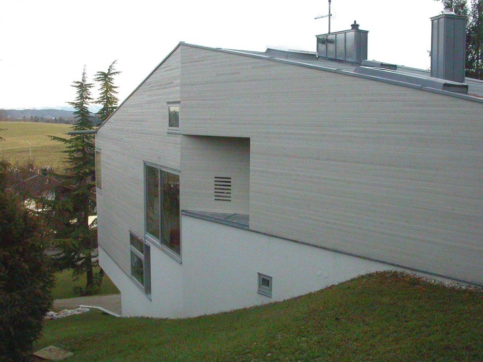 Photo of a large and gey modern concrete detached house in Munich with three floors and a pitched roof.
