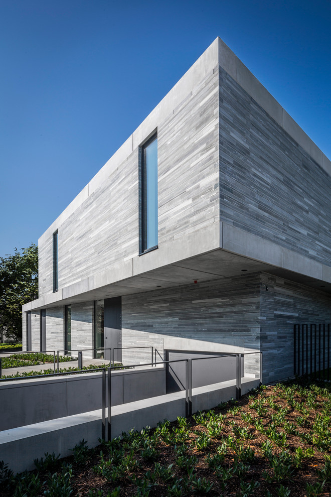 Réalisation d'une façade de maison grise minimaliste en pierre à un étage avec un toit plat.