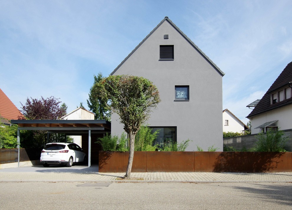 Foto på ett mellanstort funkis grått hus, med två våningar, stuckatur, sadeltak och tak med takplattor