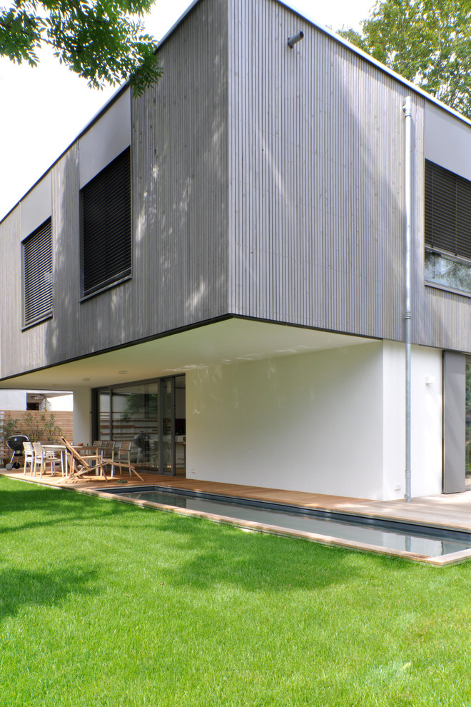 Cette image montre une grande façade de maison grise design en bois à un étage avec un toit plat.