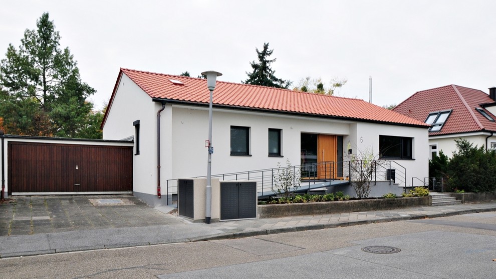 На фото: двухэтажный, белый частный загородный дом в современном стиле с облицовкой из цементной штукатурки и черепичной крышей с
