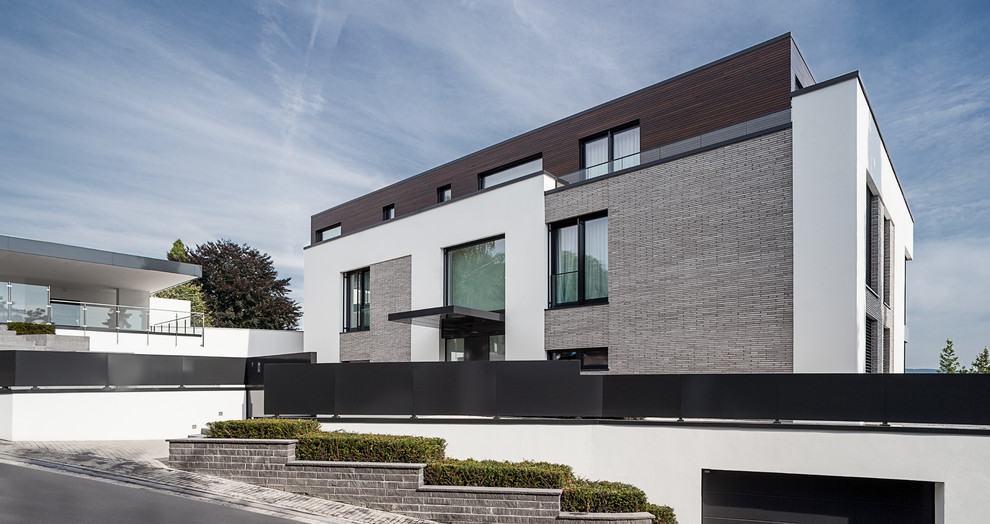 Expansive and gey contemporary house exterior in Other with three floors, stone cladding and a flat roof.