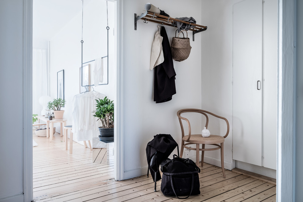 Foto på en liten minimalistisk hall, med vita väggar, ljust trägolv och beiget golv