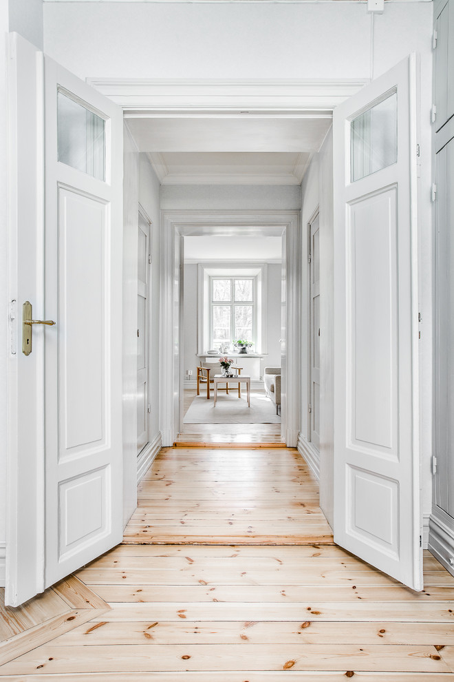 На фото: большой коридор в скандинавском стиле с белыми стенами и светлым паркетным полом с