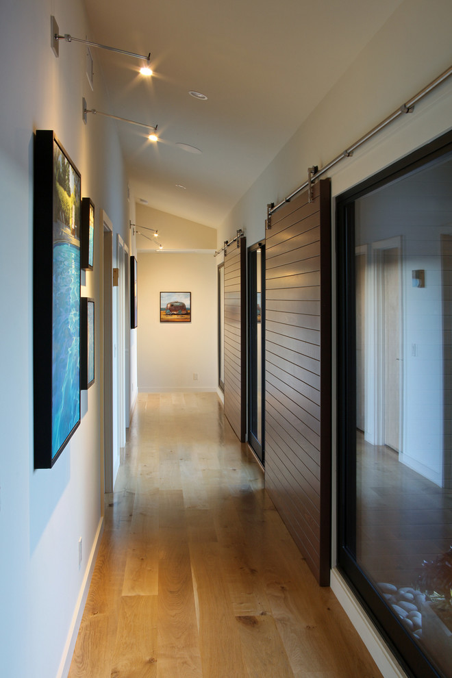 Exemple d'un couloir moderne de taille moyenne avec un mur blanc, parquet clair et un sol marron.