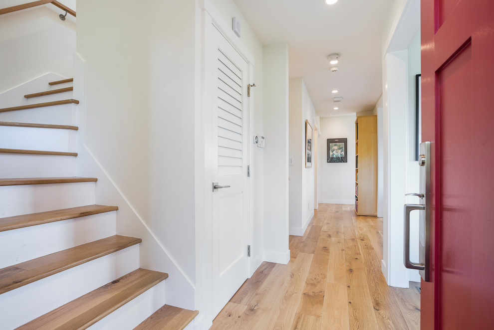 Cette image montre un grand couloir traditionnel avec un mur blanc, un sol en bois brun et un sol marron.