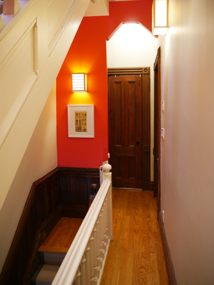 Cette image montre un petit couloir victorien avec un mur rouge et un sol en bois brun.