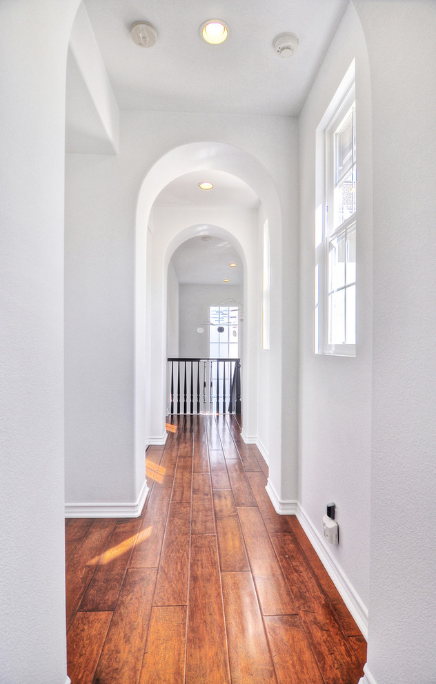 Inspiration pour un couloir design avec un mur blanc et un sol en bois brun.