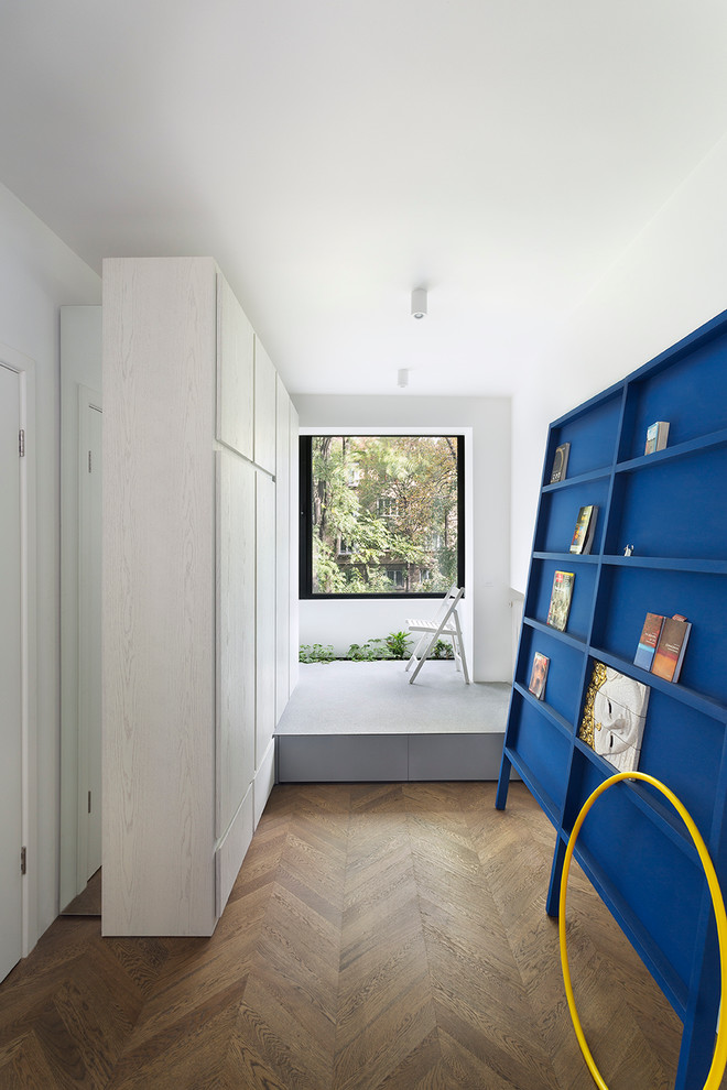 Idée de décoration pour un couloir design avec un mur blanc et un sol en bois brun.