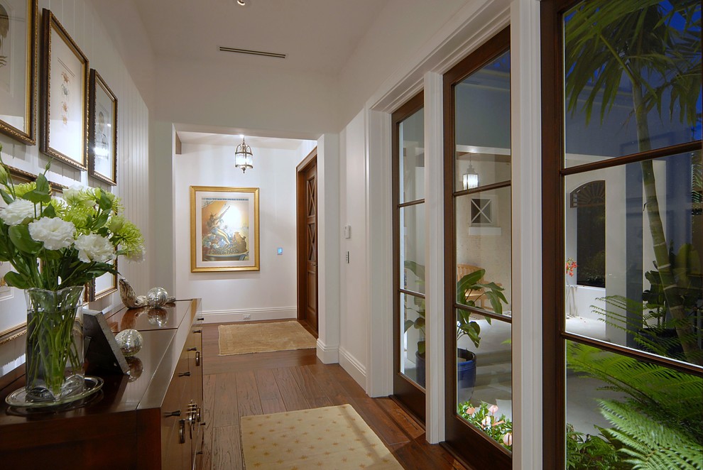 Example of a mid-sized island style medium tone wood floor and brown floor hallway design in Miami with white walls