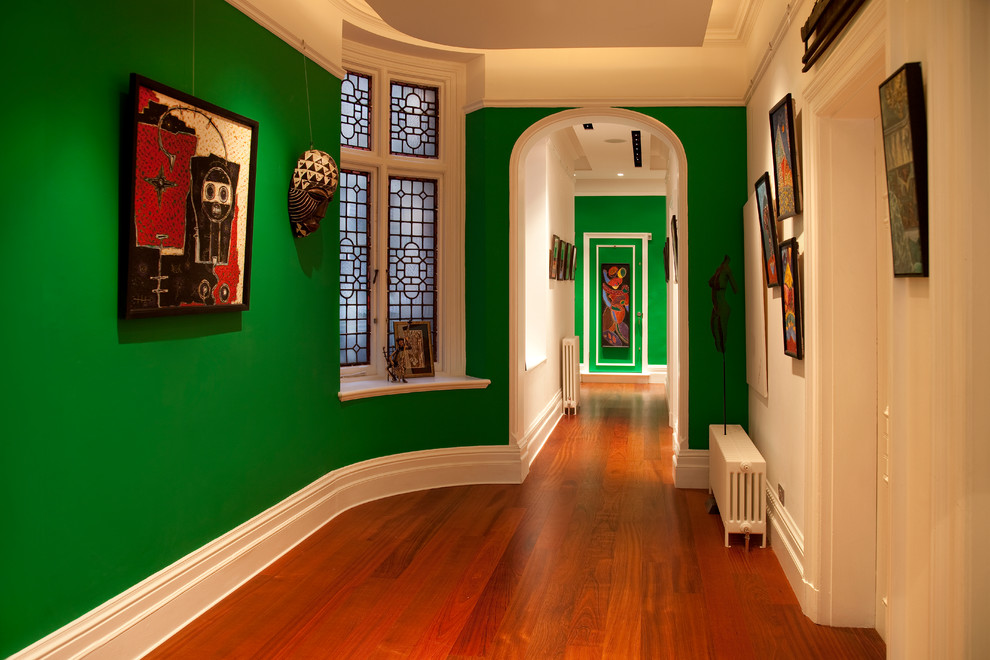 Réalisation d'un grand couloir bohème avec un mur vert et un sol en bois brun.