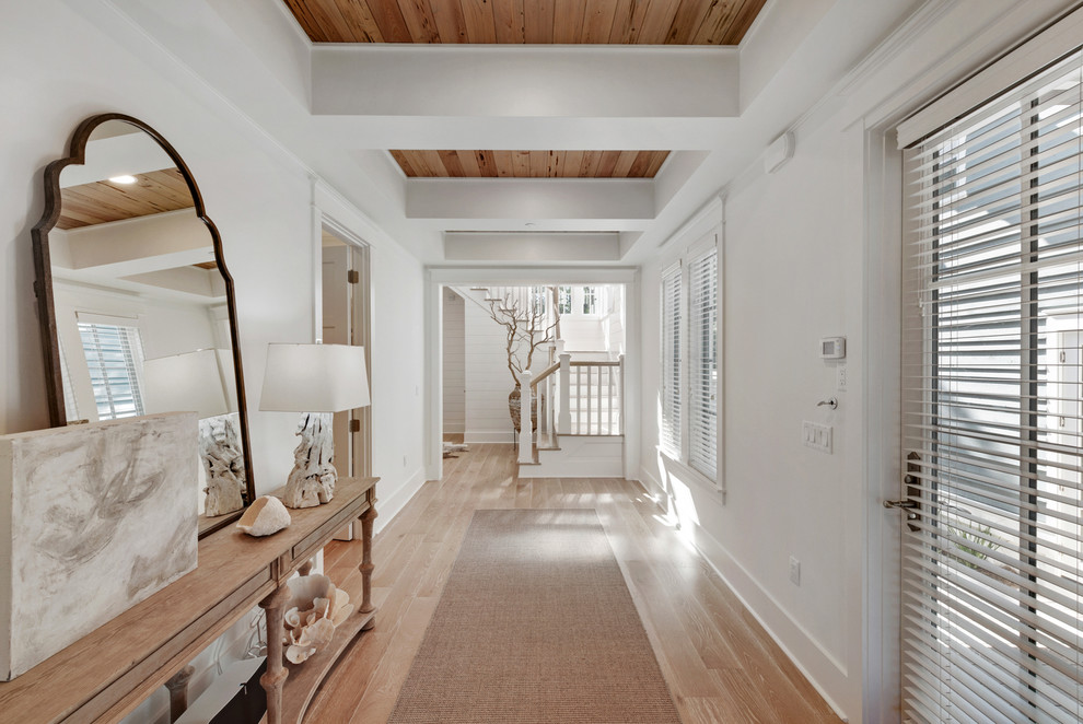 Ejemplo de recibidores y pasillos costeros con paredes blancas, suelo de madera en tonos medios, suelo marrón y iluminación