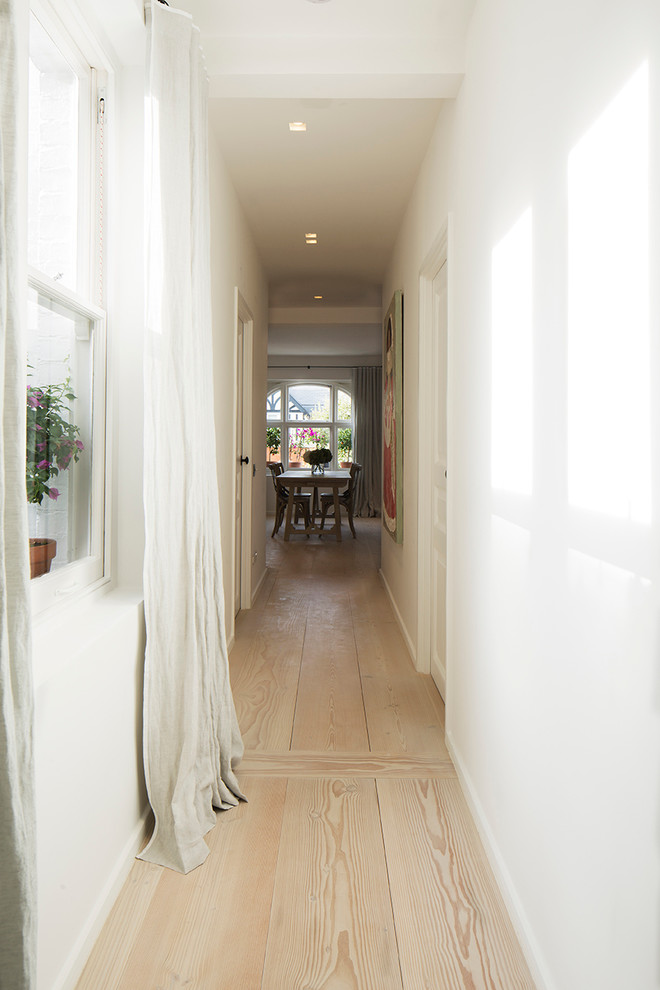 Large trendy light wood floor and beige floor hallway photo in London with white walls