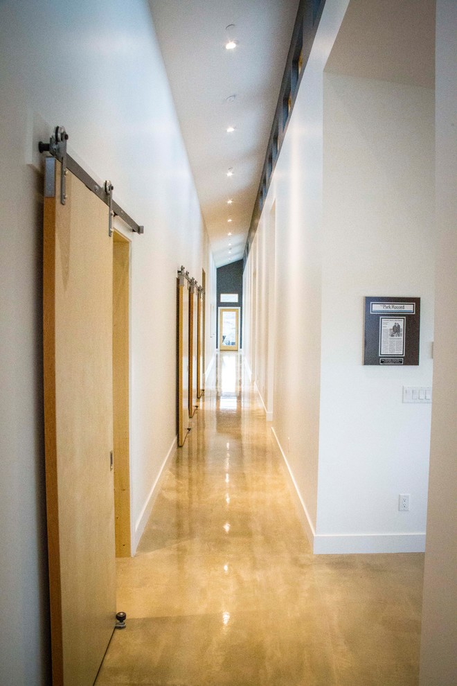 Aménagement d'un couloir moderne avec un mur blanc, sol en béton ciré et un sol marron.