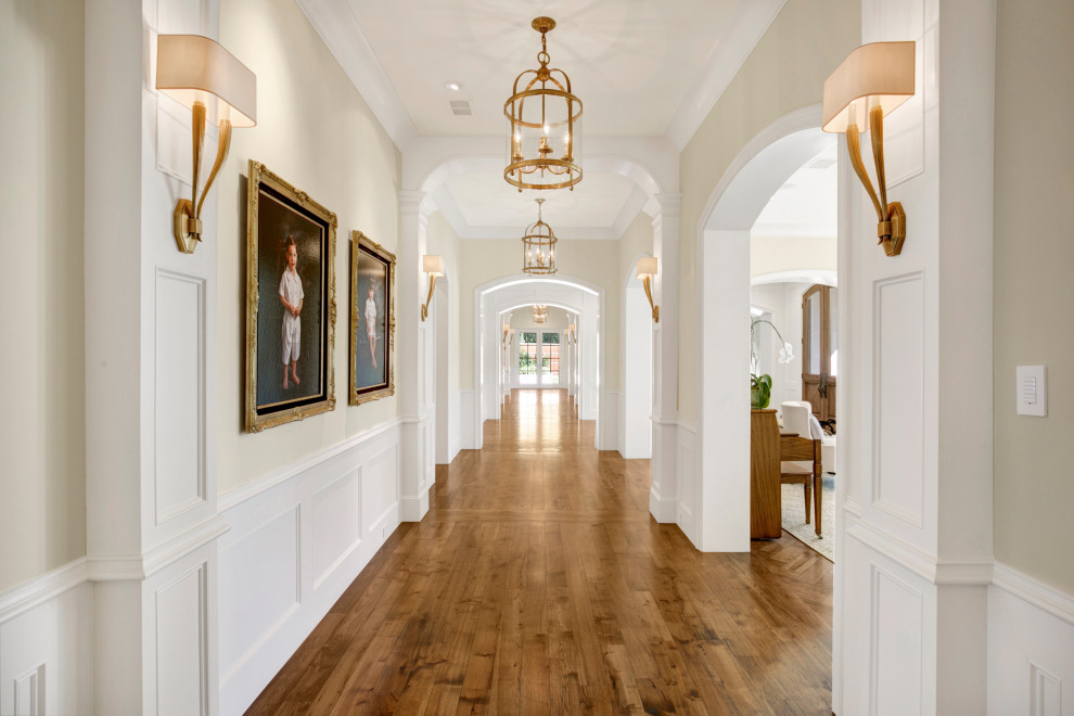Immagine di un grande ingresso o corridoio con pareti bianche, pavimento in legno massello medio, pavimento marrone e boiserie